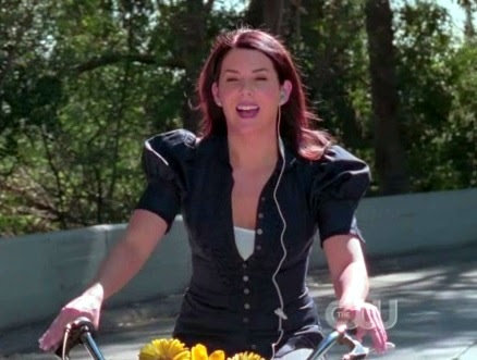 Lorelai riding her bike wearing a wired earpiece